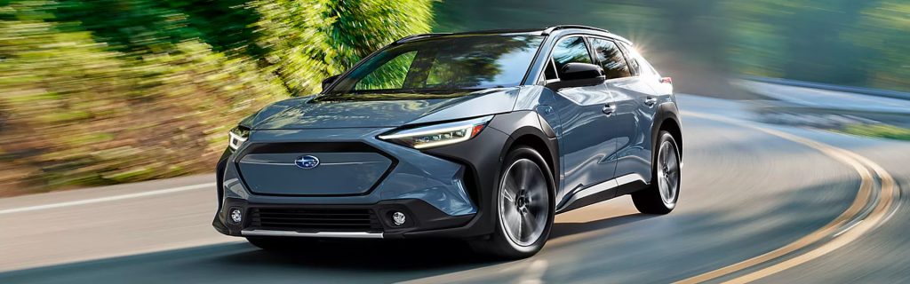 A Subaru Solterra driving on a curved road surrounded by greenery.