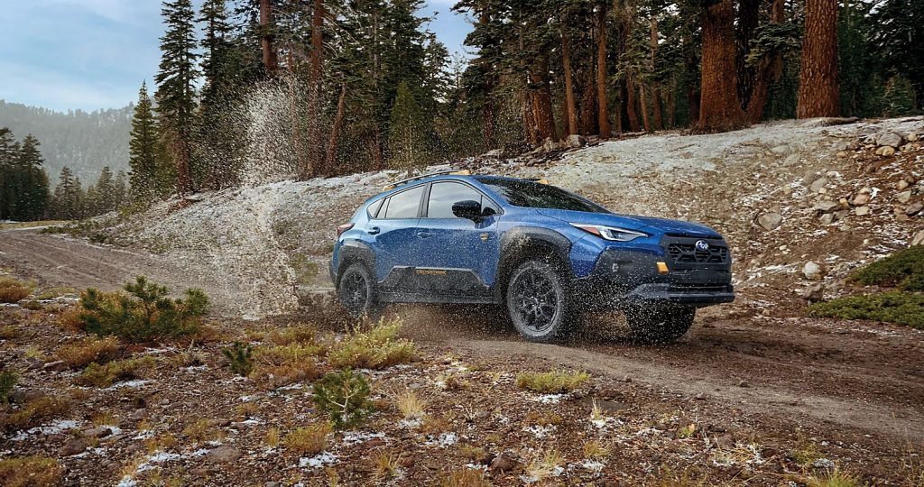 Blue Subaru Crosstrek driving through a muddy forest trail.