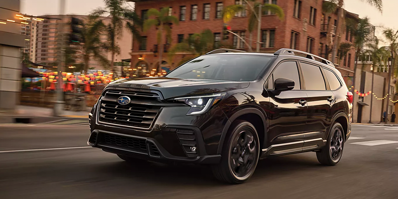 Black Subaru SUV driving through a city street with motion blur and urban buildings in the background.